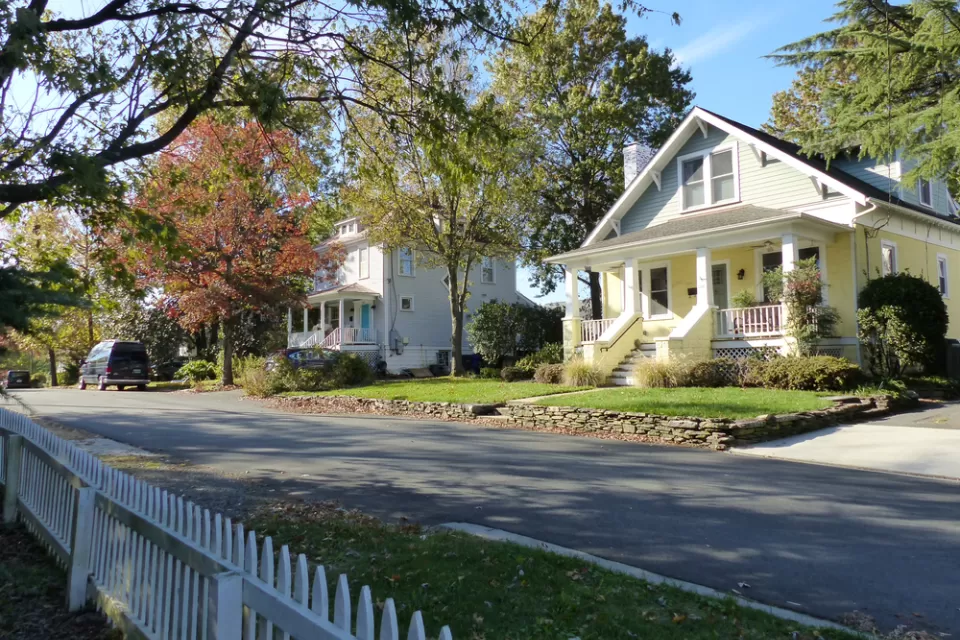 Large historic homes and white picket fences line a street.